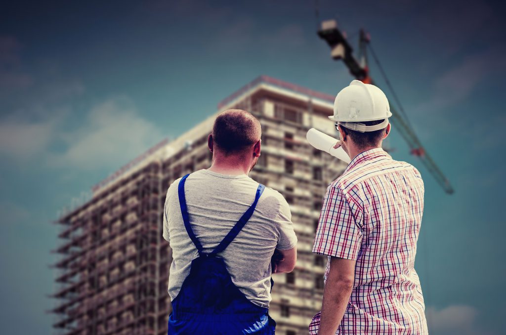 建設途中のマンションを見つめながら会話する2人の男性